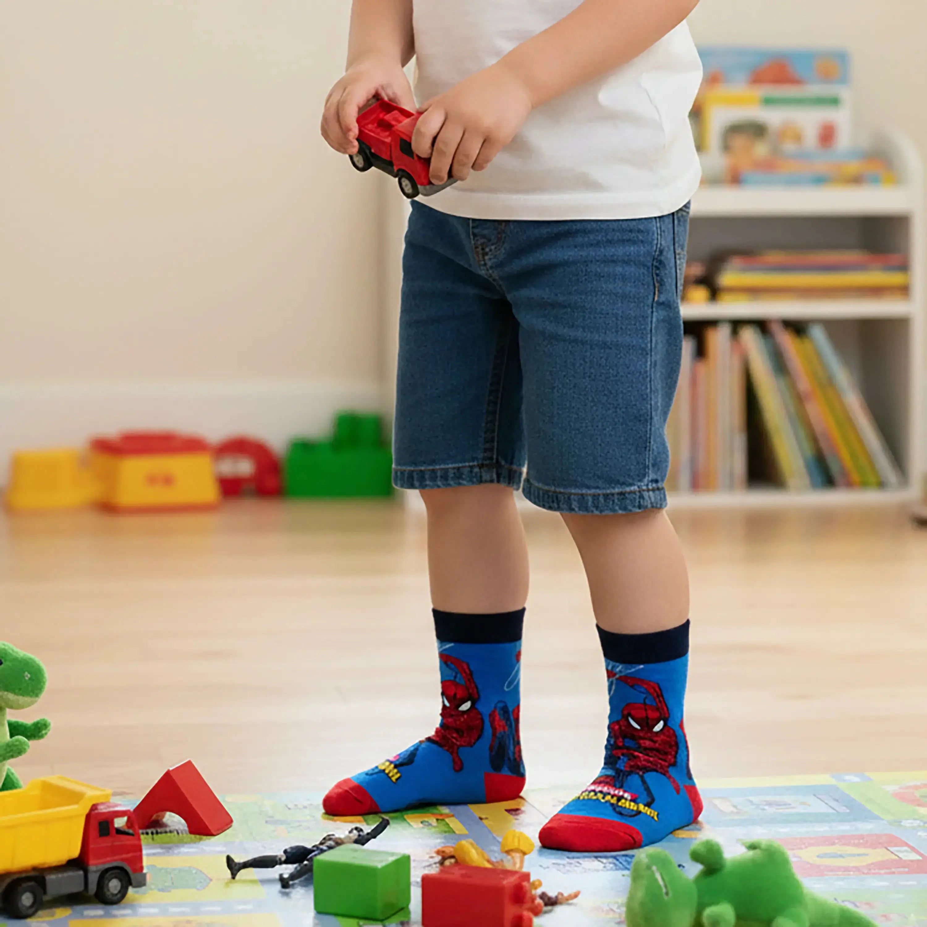 An image of a boy wearing Supersox Marvel Spider-Man Blue and Red Printed Crew Socks while standing and playing with toy cars in a playroom