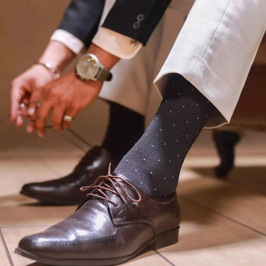 An image of a man wearing grey patterned formal socks with brown leather dress shoes and dark trousers. 3243