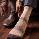 An image of a man wearing grey formal socks with a subtle pattern, styled with tan trousers and a brown leather chair.